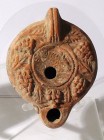 A ROMAN TERRACOTTA OIL LAMP 2nd-4th century CE. 9.1 cm. Shoulders covered with grapes and the center depicts a fish. With a crack at the handle but in...