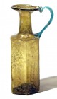 A HEXAGONAL TRANSLUCENT YELLOW GLASS JUG WITH A GREEN HANDLE 6th-7th century CE. 18.8 cm high. Blown in a mold, depicts a column on each side. With an...