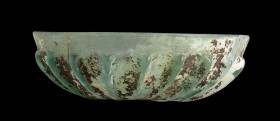ROMAN GLASS RIBBED BOWL
1st -3rd century AD
height cm 4,5; diam. cm 15,3

Beautiful ribbed bowl of a trasparent bluish-green glass, with sporadic ...