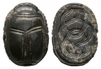 Second Intermediate Period, c. 1650-1550 B.C. Black hardstone scarab (15x11mm). Base engraved with a coiled cord pattern. Intact with some deposits, p...