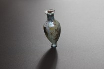 Colorless glass amphoriskos. Eastern Mediterranean, 1st-2nd cent. AD. (63.9mm x 29.8mm). Tapered body, long cylindrical neck, two handles missing, tra...