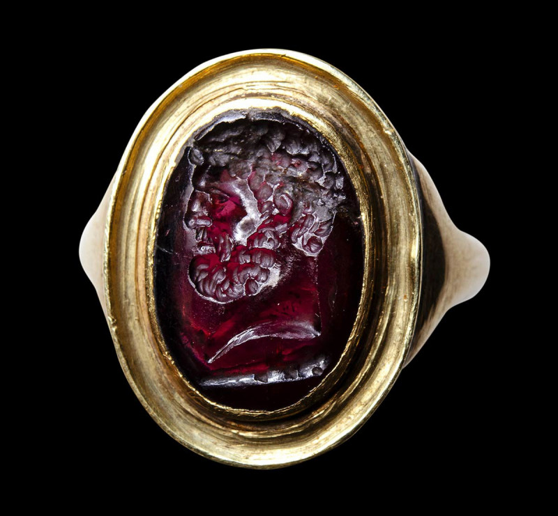 A roman garnet intaglio mounted on a Grand Tour gold ring. Bust of Hercules.

...