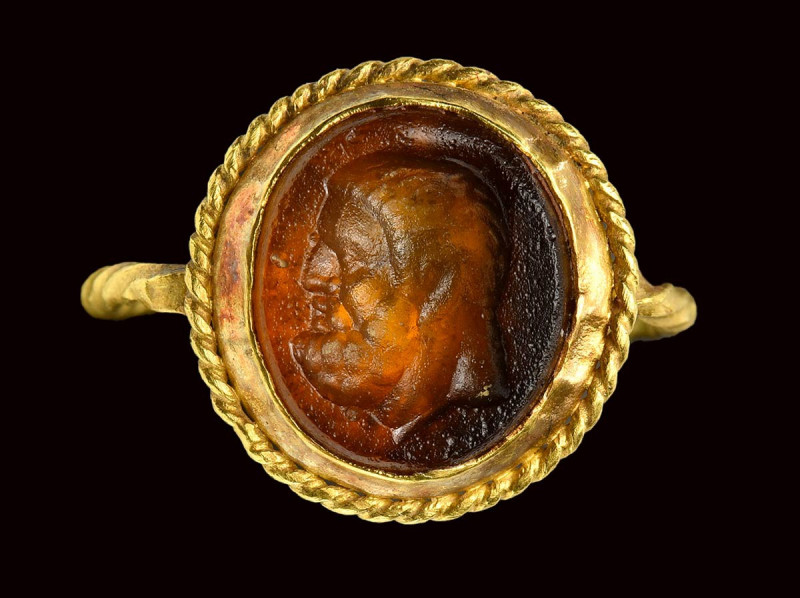 A roman orange glass paste intaglio, mounted on an ancient gold ring. Head of He...