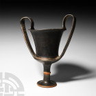 Greek Black Ware Kantharos. 5th-4th century B.C. A black ware kantharos with two integral high handles, collared stem and discoid foot. 562 grams, 27 ...