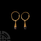 Greek Gold Garnet Drop Earrings. 5th-3rd century B.C. A matched pair of gold earrings, each composed of a tapering round-section hoop and inverted con...