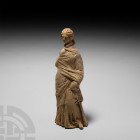 Greek Terracotta Standing Figure. Early 3rd century B.C. A terracotta figure modelled in the round, standing, wearing full length robes held by one ha...