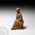 Greek Seated Terracotta Female Figure of a Muse. 3rd century B.C. A terracotta female figure modelled seated, wearing a full-length robe, one shoe eme...