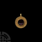 Gold Pendant with Garnet. Early 1st millennium A.D. A gold discoid pendant ornamented with alternating bands of applied pellets and ropework, raised c...