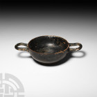 Greek Kylix. c.4th century B.C. A ceramic miniature blackware kylix, composed of a U-section body, two handles placed high on the neck and basal ring....
