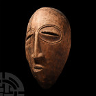 Kenyan Kamba Tribal Mask. 20th century A.D. A wooden mask, hollow to the reverse, with reserved hoops around the eye-slots developing to a slender nos...