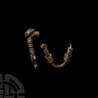Near Eastern Fibula Group 7th century B.C. A pair of artefacts comprising: a fragment of a triangular fibula, the surviving arm decorated with grooves...