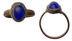 Roman Ring with Blue Stone. Bronze Æ (2.9 gr.), 1st - 2nd Century AD. A ring with slender round-section hoop, oval-shaped bezel with raised cell set w...