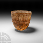 Roman Clear Cut Glass Beaker
Circa 4th century A.D. A translucent glass beaker or other vessel with wheel-cut bands creating registers of ellipses an...