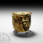 Roman Glass Beaker with Blue Stipples
Circa 4th century A.D. A U-shaped pale green glass beaker or lamp with convex wall and convex everted rim; appl...