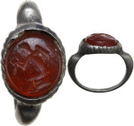 A carnelian intaglio ring. Roman, c. 2nd cent AD. Red. Round bezel: 11 mm. The gem is set in a silver ring. D-sectioned hoop, expanding at the shoulde...