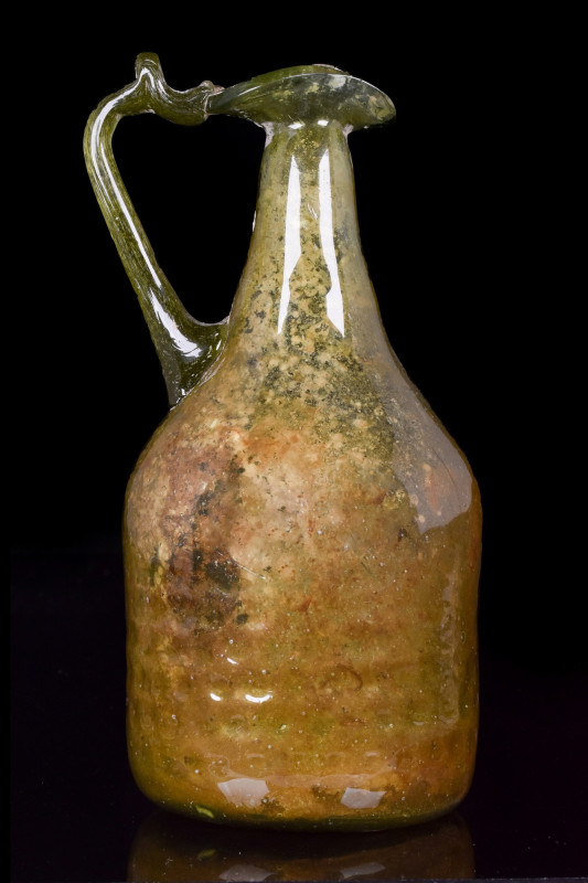 ROMAN GLASS JUG
Ca. 200-300 AD. 
A one-handled jug in a translucent green pale...