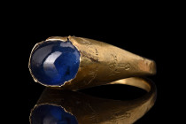 SELJUK GOLD RING WITH LARGE BLUE SAPPHIRE AND KUFIC INSCRIPTION 

 Ca. 1100-1200 AD
 A gold ring with a stirrup profile, and a thin hoop expanding ...