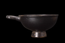 APULIAN BLACK GLAZE CUP WITH HANDLE

 Ca. 400-300 BC
 A ceramic cup featuring a deep cup mounted on a flared foot, adorned with a lustrous black gl...