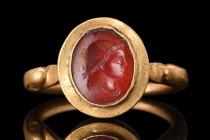 ROMAN GOLD RING WITH CARNELIAN PORTRAIT INTAGLIO 

 Ca. 300 AD
 A gold finger ring with its band formed into a hoop with duck-head finials, which a...