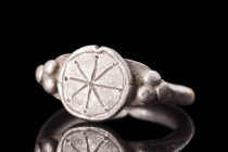 ROMAN SILVER RING WITH WHEEL OF FORTUNE PATTERN 

 Ca. 100-300 AD
 A captivating silver ring formed from a round hoop. The ring boasts finials that...