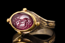 EARLY MEDIEVAL GOLD RING WITH ROMAN GARNET DOG INTAGLIO 

 Ring ca. 600-700 AD; Stone - ca. 200 AD
 A gold ring of a flat-section hoop, with its gr...