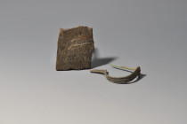 ROMA. Lote de 2 objetos: fíbula de arco y fragmento de placa con inscripción (ss. III-IV d.C.). Bronce. Longitud de 5 a 5,5 cm.