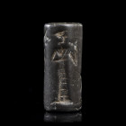 *SCEAU-CYLINDRE
En hématite figurant un arbuste dans un vase encadré par de part et d'autre par un personnage masculin en intercession et un étendard...