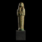 CHAOUABTI 
En faïence verte et noire, figuré dans sa gaine mommiforme; perruque tripartite. Les mains croisées tiennent les instruments aratoires (pe...