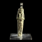 CHAOUABTI 
En faïence siliceuse à glaçure vert clair et noire. Dans sa gaine momiforme; perruque tripartite et colonne hiéroglyphique sur le corps ; ...