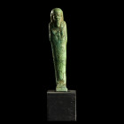 USHABTI
En faïence siliceuse à glaçure verte. 
Dans sa gaine mommiforme ; perruque tripartite et barbe postiche ; instruments aratoires et colonne d...