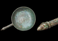 ROMAN BRONZE PATERA WITH RAM HANDLE

 Ca. 1-300 AD
 A bronze patera featuring a round bowl with a mid-depth profile, a flat base, and a pronounced ...