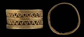 An etruscan gold ring. The hoop has a large and flat band, with an intertwined decoration, alternating with a serpentine, threadlike element on two le...