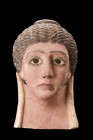 Roman Period, ca. 30 BC - 323 AD.
A moulded ceramic funerary mask of a youthful female with braided hair drawn to the top of the head, painted detaili...