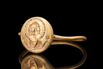 Ca. 600 AD.
A gold ring comprised of a thin round-section hoop, and an applied circular bezel that is adorned with a representation of the bust of the...