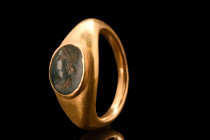 Ca. 100-200 AD.
A gold finger ring composed of a hollow hoop, expertly formed to expand and support a large oval bezel cell. This cell is set with a f...