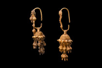 Ca. 100-200 AD.
A magnificent pair of gold earrings featuring oval-shaped, round-section hoops, each adorned with an array of finely wrought floral pl...