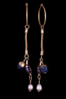 Ca. 600 AD.
A matched pair of gold earrings, each a tapering hoop, hook-and-clasp closure, and a single elongated pendant comprising glass and pearls ...