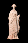 Ca. 400-300 BC.
Tall molded terracotta standing female figure, wearing a floor length layered drapery garment. Head turned slightly to the right havin...