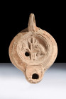 Ca. 1-100 AD.
A terracotta oil lamp boasting a recessed tondo adorned with a dolphin in front of a rudder. The dolphin, a recurring motif in ancient R...