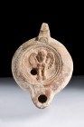 Ca. 100-300 AD.
A moulded pottery oil lamp with a small spout and recessed tondo featuring relief depiction of a harpy and a slightly off-centre filli...