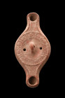 Ca. 300-400 AD.
A mold-made terracotta oil lamp featuring a circular body that is prolonged by two round-tipped nozzles, one at the opposite end, crea...