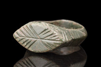 Ca. 100-300 AD.
A bronze finger ring featuring a round hoop, exhibiting a slight carination that adds a subtle visual distinction. The shoulders of th...