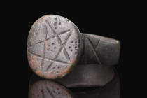 Ca. 400-500 AD.
A bronze finger ring composed of a flat-section hoop and a circular bezel adorned with intricate dotted patterns and a prominent penta...