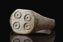 Ca. 200-500 AD.
A bronze ring with a round hoop, supporting a flat bezel decorated with a set of four irregularly placed 'ring and a dot' patterns, pr...