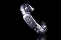 Ca 1200 AD .
A fine silver bracelet of a penannular type with applied rectangular-shaped panels with round edges and engraved borders. Both ends of th...