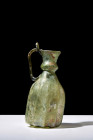Ca. 1200 AD.
A glass ewer in a distinctive greenish tone. This vessel boasts a bell-shaped lower body distinguished by an intricate facetted adornment...