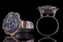 European, ca. 1400 AD.
An exquisite silver gilt finger ring featuring a beautiful floral-shaped bezel with raised bosses and remnants of blue and gree...