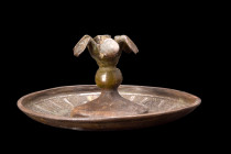 Ca. 1100-1200 AD.
A bronze lid with a round shape features a recessed upper face, with a thick decorative band with silver inlaid decor. This band enc...