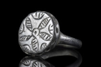 Ca. 500-600 AD.
A beautiful bronze ring with a smooth, circular band supporting a large bezel decorated with a five-petaled floral design. Further inc...