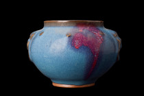 .
A Jun porcelain vessel featuring a bulbous body and unglazed foot, raised mouth, and relief handles in the shape of a face with a hanging loop benea...
